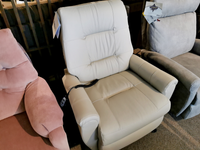 A white Felicia Lift Chair by Best, featuring a modern design and a convenient control remote, is gracefully placed between pink and gray chairs in the showroom. Its Space Saver feature ensures it fits perfectly in any room.