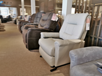 A row of recliner chairs in various colors is displayed in the furniture store, showcasing a modern touch. In the foreground, a white Felicia Lift Chair by Best with Space Saver feature invites relaxation and style.