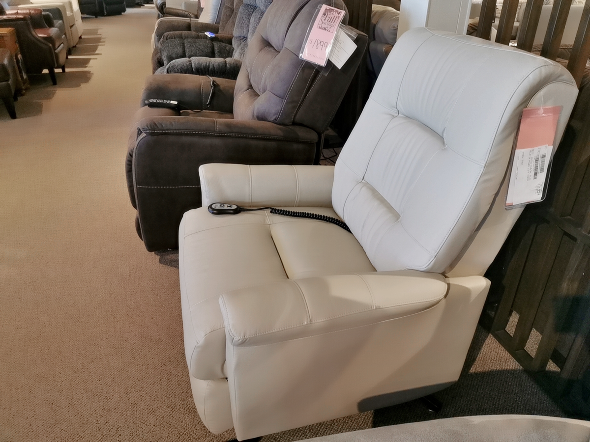 A row of recliner chairs is displayed in a furniture store, featuring a modern white leather Felicia Lift Chair by Best in the foreground.