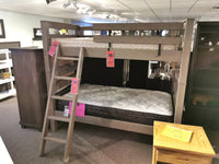 The Crate S43905 Twin Bunkbed is elegantly displayed in the showroom, boasting a sturdy Southern Yellow Pine TimberFrame with tags hanging. It features a convenient ladder and two plush mattresses.