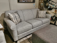 The Decor-rest 2963 Sofa, an elegantly gray upholstered transitional piece complete with two patterned throw pillows, is meticulously designed for smaller spaces and displayed in a furniture store showroom.