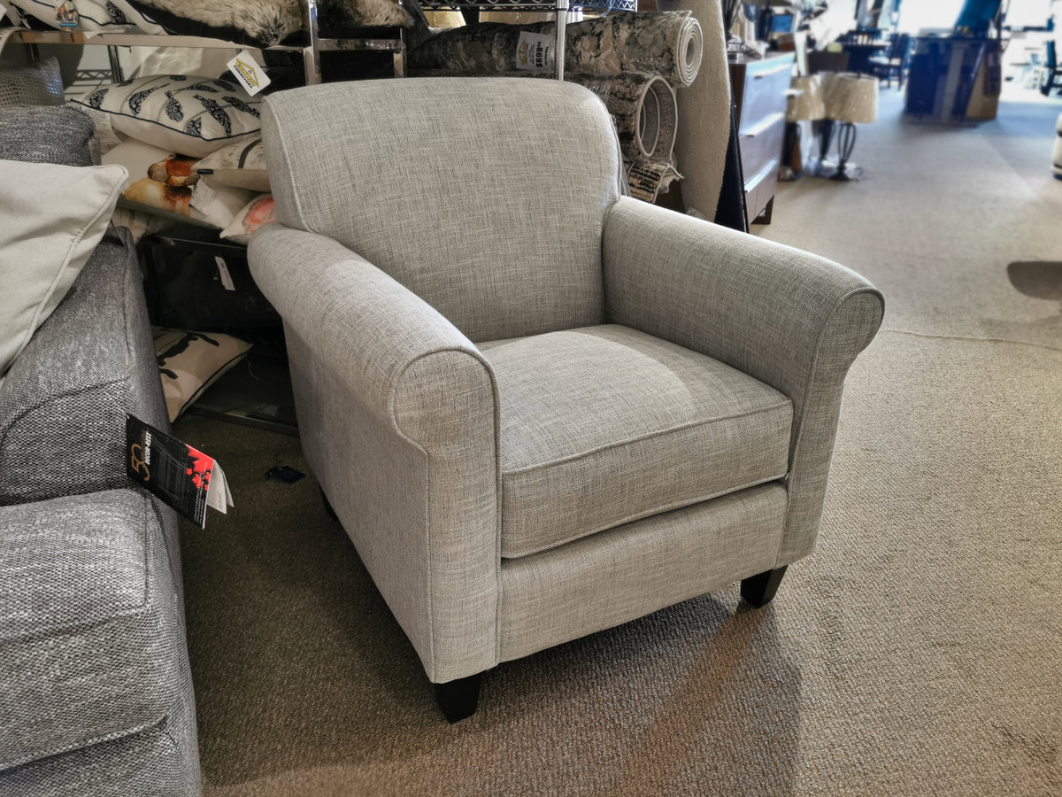 The Decor-rest 2963 Chair, with its timeless gray upholstery, is displayed on a carpeted floor in a furniture store, ideally complementing smaller spaces.