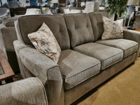 The Decor-rest 2967 Sofa, showcasing a contemporary style in brown fabric with customizable options, features three cushions and two floral pillows, displayed next to a wooden side table in a furniture showroom.