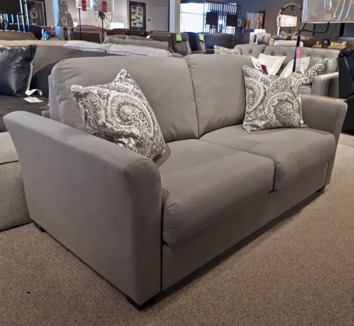 The Decor-rest 2T5 'Transformer' Double Sofa Bed, on display in a furniture store, showcases a gray design with patterned cushions and features a fire-retardant mattress, blending style with safety.