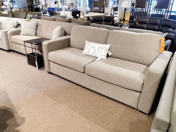 A showroom features a light gray Decor-rest 2T3 Queen Transformer Sofa Bed adorned with a "love" pillow, surrounded by other couches on the carpeted floor.