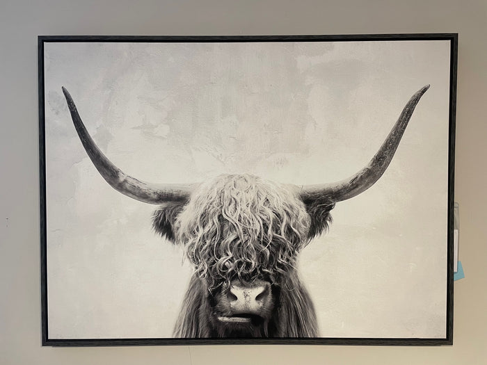 The Pancho Wall Art by Ashley masterfully captures the essence of a Highland cow with its long curved horns prominently displayed. This black and white photograph is beautifully set against a light background and elegantly enclosed in a sleek black frame.