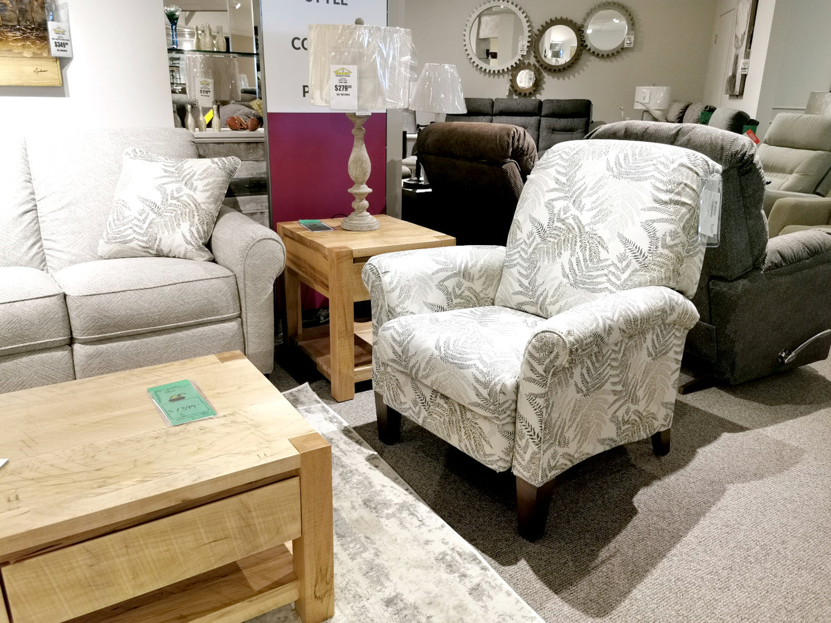 Explore our furniture showroom, showcasing a patterned armchair, light gray sofa, wooden coffee table, and side table with two lamps. Don't miss the cozy 424 Fletcher Hi-Leg Recliner by La-Z-Boy, a proud addition made in America to elevate your comfort and style.