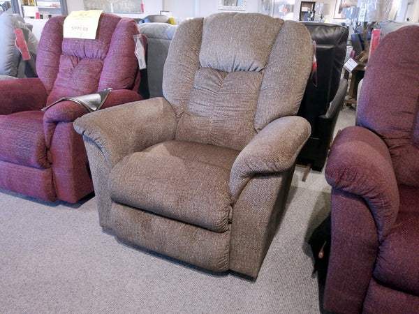 The furniture store showcases the La-Z-Boy 709 Jasper Rocker Recliner with its brown upholstery, flared pillow arms, and ultra-plush chaise seat, surrounded by other inviting recliners.