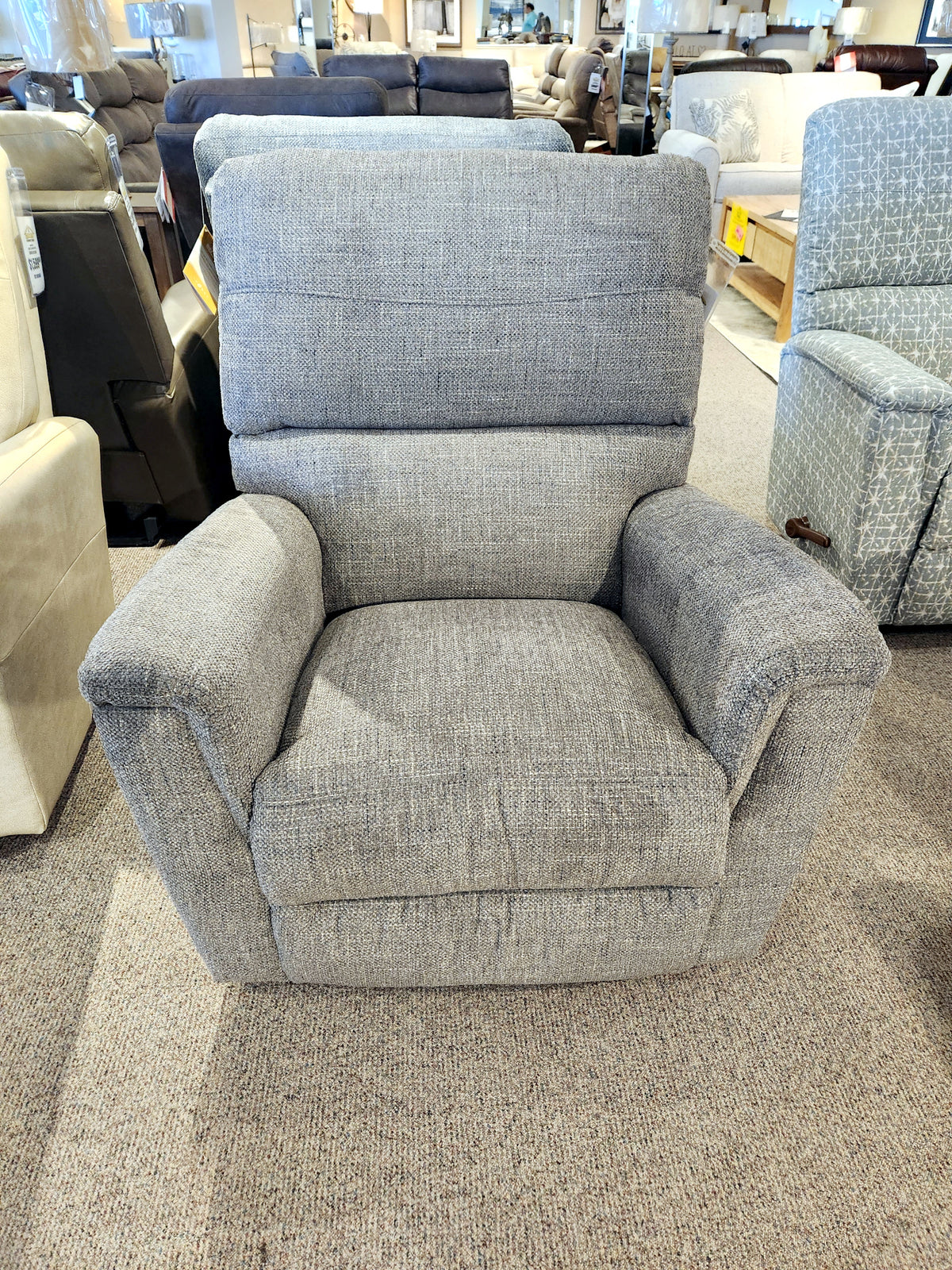 The 769 Ava Rocker Recliner by La-Z-Boy, featuring adjustable support, is displayed on a beige carpet in a furniture showroom.