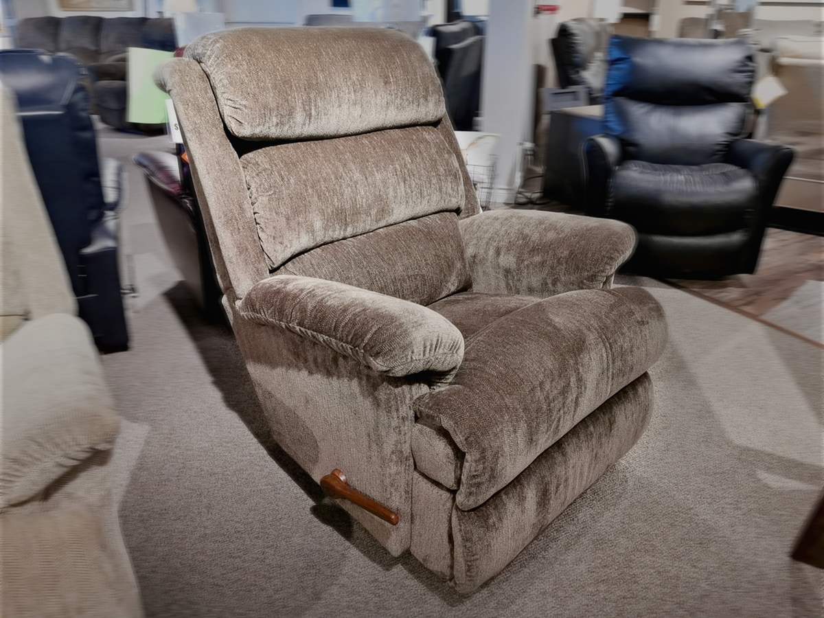 In a furniture showroom, the luxurious 519 Astor Rocker Recliner by La-Z-Boy, featuring a wooden lever and tall frame, graces the carpeted floor.