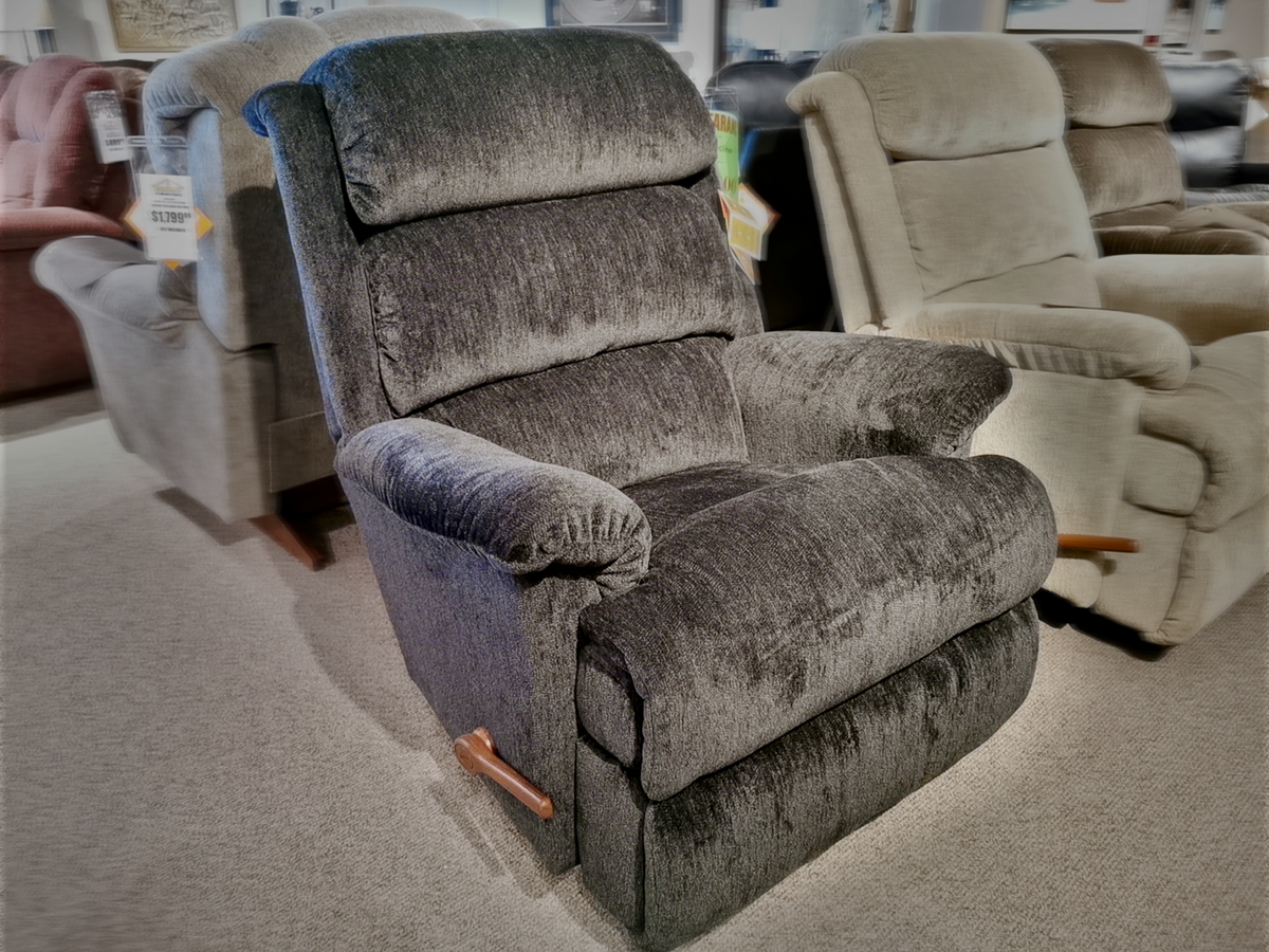 A black upholstered 519 Astor Rocker Recliner by La-Z-Boy, featuring elegant wood handles, is showcased in the furniture store.