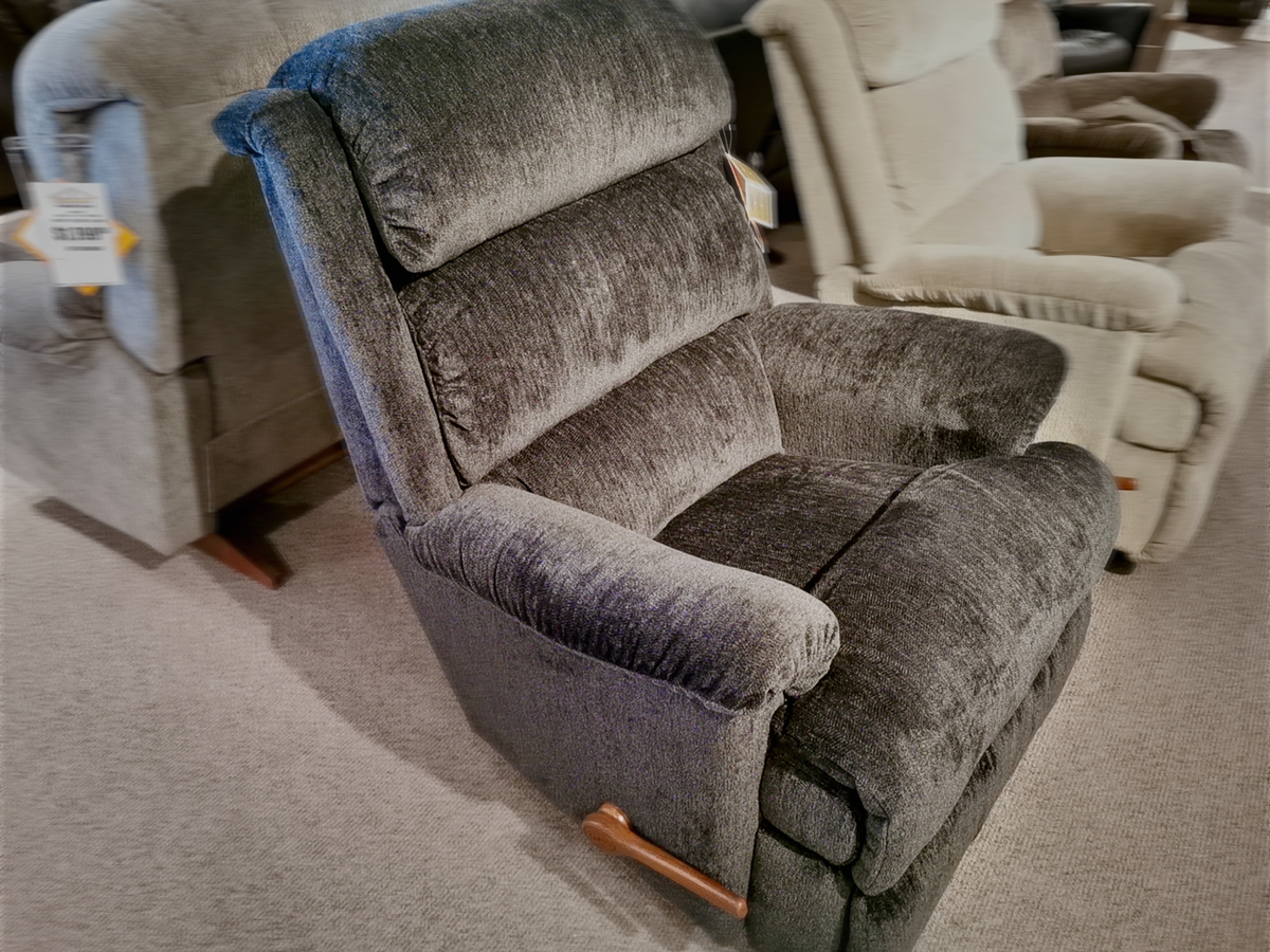 The 519 Astor Rocker Recliner by La-z-boy, a plush gray marvel, is featured in the showroom alongside a variety of other seating options. This tall recliner guarantees unparalleled comfort and sophistication for any living space.