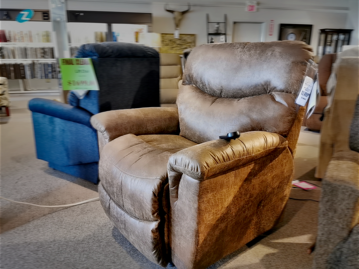 The La-Z-Boy 521 James Luxury Lift Chair, a brown recliner featuring a remote on the armrest, is elegantly showcased in a furniture store. Its space-saving design enhances any living room decor, beautifully complemented by a blue chair in the background.