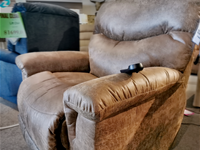 A 521 James Luxury Lift Chair from La-Z-Boy, featuring a remote on the armrest, is displayed in a furniture store setting, showcasing its space-saving design in a large brown color.