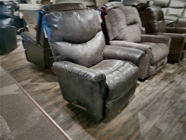 In the furniture store showroom, the La-z-boy 521 James Rocker Recliner, with its sleek black leather and bucket-style seat, stands out on the wooden floor, featuring advanced PowerReclineXR technology alongside other reclining chairs.