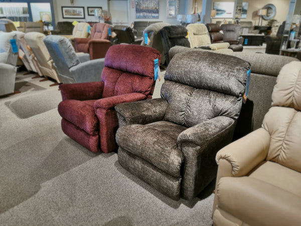 A showroom featuring an exquisite range of ultra-plush casual recliners, including the La-Z-Boy 704 Reed Rocker Recliner, showcases models in red, gray, and beige upholstery. Each piece is designed to provide a seamless comfort zone for the ultimate relaxation experience.