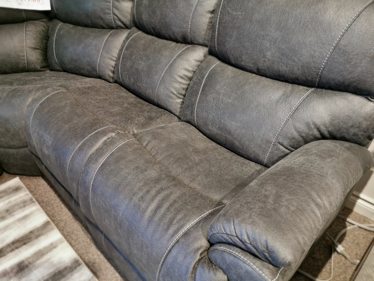 The 724 Trouper Reclining Corner Sectional by La-Z-Boy, in dark gray leather with visible stitching and bucket seats, is placed on a carpeted floor next to a striped rug.