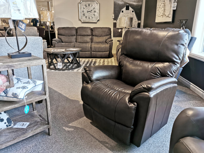 The La-z-boy 724 Trouper Leather Rocker Recliner, featuring lumbar support and a contemporary brown leather finish, is showcased in a furniture store showroom amidst various sofas and home decor items.