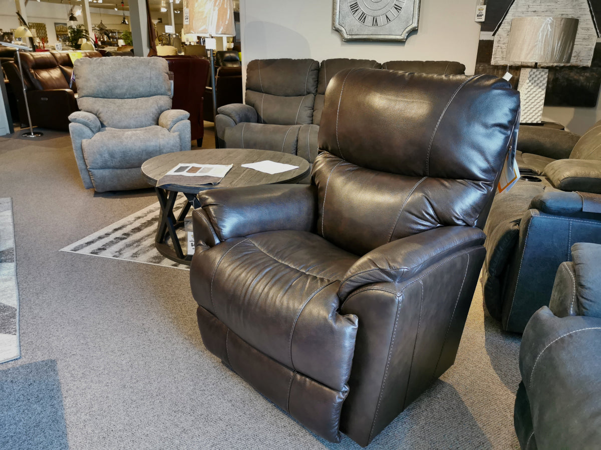 The 724 Trouper Leather Rocker Recliner by La-Z-Boy is featured in a furniture showroom beside other chairs and a round wooden table, presenting the perfect combination of comfort and style with its modern design and integrated lumbar support.