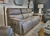 La-z-boy's 724 Trouper Reclining Sofa set in gray showcases plush bucket seats in a living room setting, enhanced by a lamp and wall art in the background.