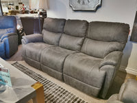 In a furniture store, the La-Z-Boy 724 Trouper Reclining Sofa in gray is showcased, offering plush bucket seats and a comfortable chaise legrest, accompanied by a clearance sale sign on the left side of the image.