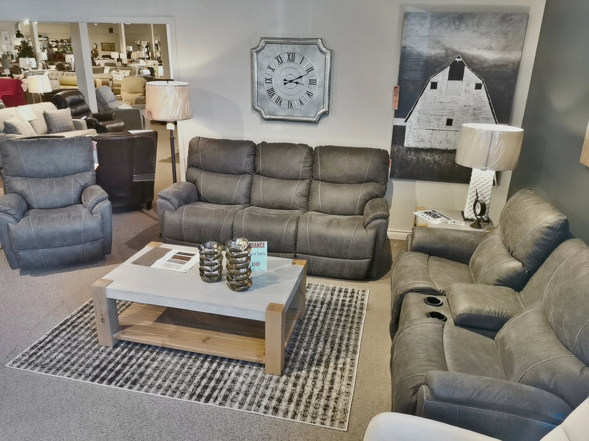 Living room display with a La-Z-Boy 724 Trouper Reclining Sofa set featuring bucket seats and a chaise leg rest, complemented by a wooden coffee table, large clock, and black-and-white barn artwork.