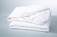 A folded Quilted Mattress Protector by Conway Furniture in white, featuring a quilted pattern and offering a comfort guarantee, rests gently on a light surface like a soft mattress protector.