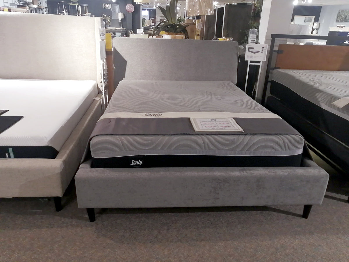 A luxury Sealy mattress on a minimalist Palliser Prairie Queen Upholstered Bed in a furniture store showroom.