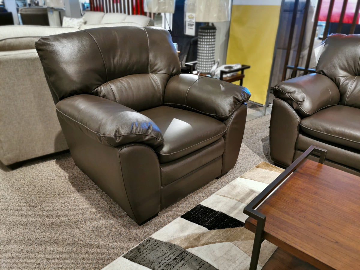 The 77343 Amisk Chair, a brown leather armchair from the Palliser brand, is showcased in a furniture showroom beside a wooden coffee table, providing lounge-like seating with exceptional comfort.