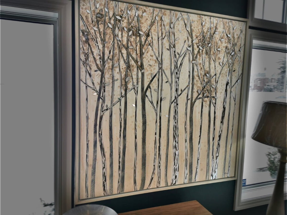 The "Winter Walk" hand-painted canvas by Renwil showcases abstract trees in brown and white tones, beautifully framed with a whitewashed floating frame. Positioned near a window, it is enhanced by acrylic mirror accents and softly lit by the glow of a nearby lamp.