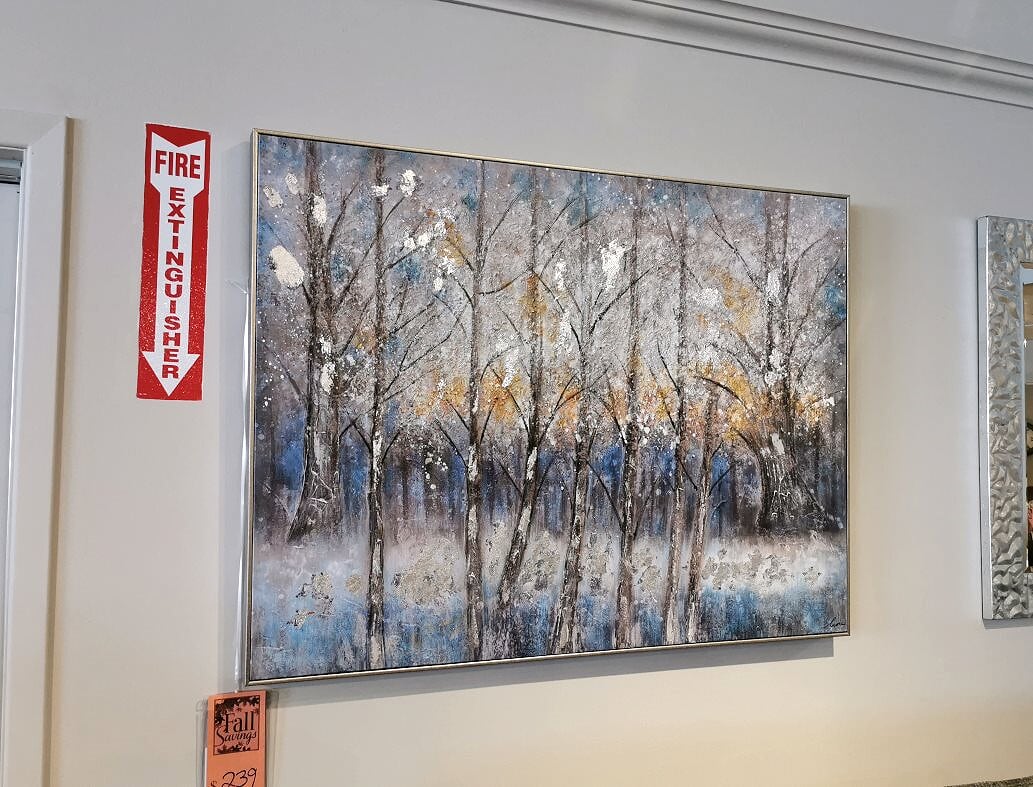 The Rast painting by Renwil, depicting a forest scene with snow-covered trees and accented with subtle touches of gold and silver leaf, is elegantly displayed on a wall next to a fire extinguisher sign.