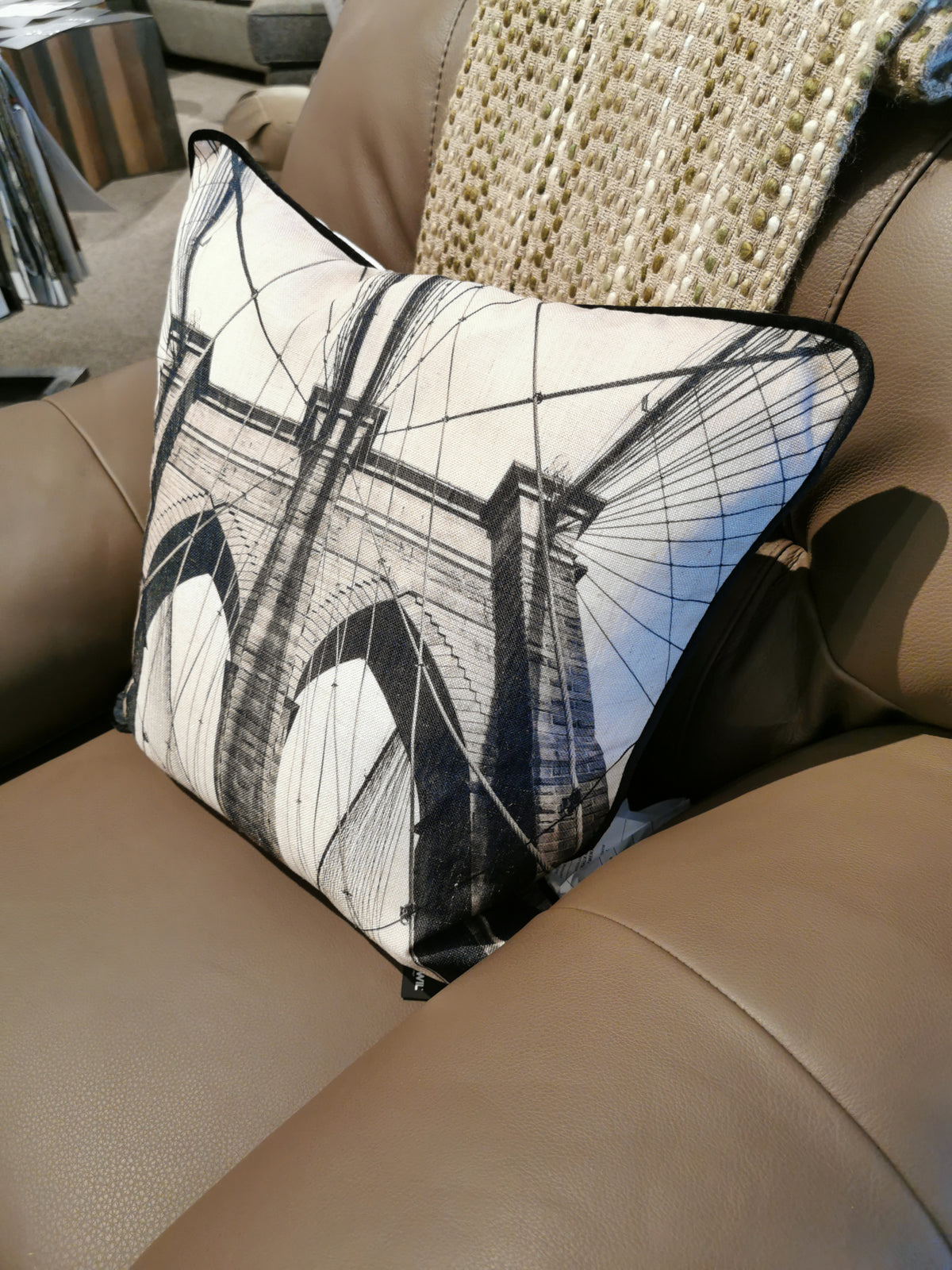 The PWFL1017 Bridge Pillow, crafted by Renwil's in-house artists, features a black and white bridge design that adds flair to the tan leather chair.