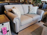 A gray Superstyle 9613 Loveseat with hardwood, includes two patterned pillows, is on sale in a furniture store.