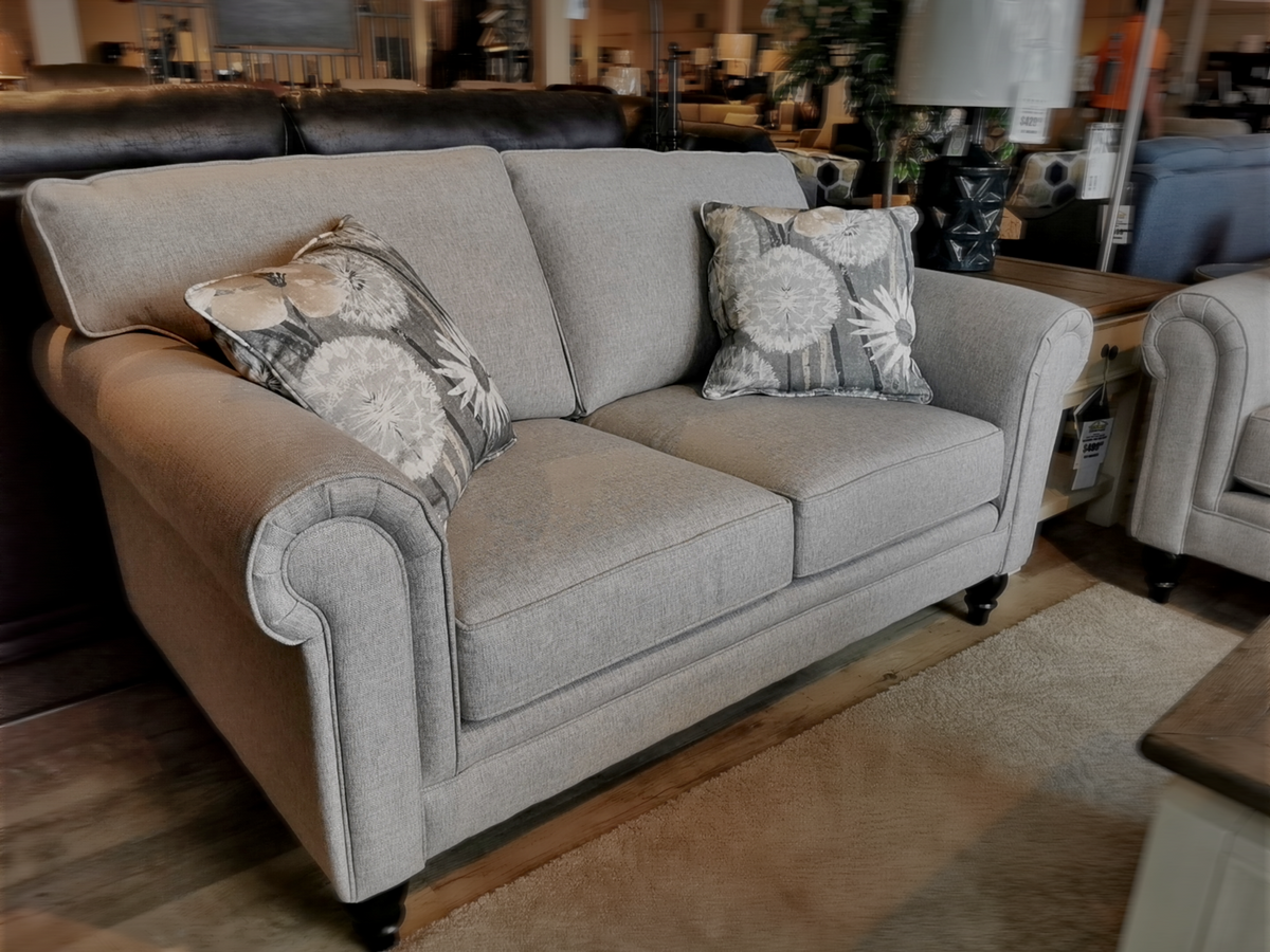 9613 Loveseat by Superstyle features rolled arms, patterned pillows, and premium foam seating on dark wood legs in a showroom.