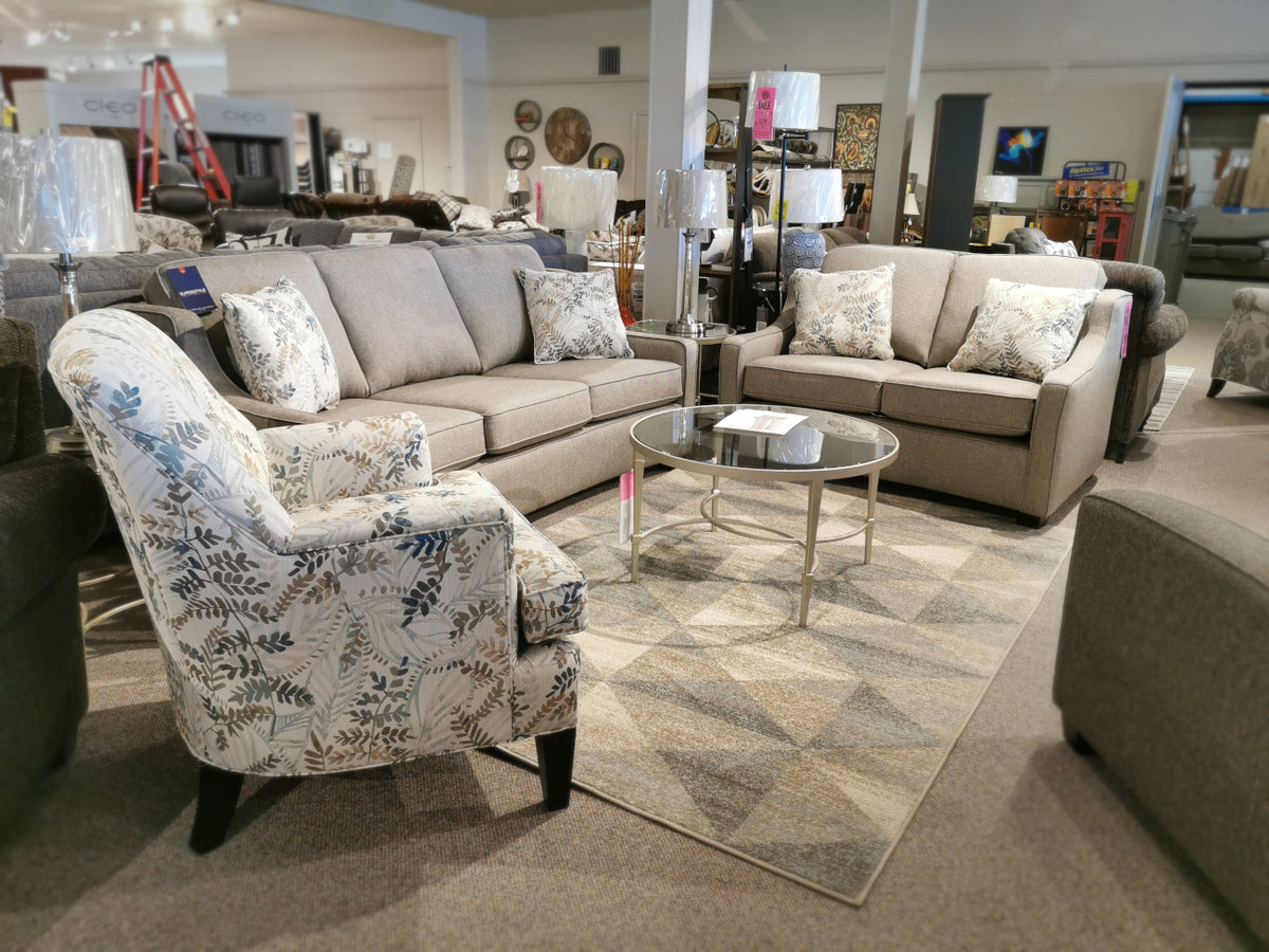 Explore a chic transitional design at our furniture showroom with the Superstyle 9670 Loveseat in beige, offering medium-firm seating, paired with a glass coffee table and an elegantly patterned armchair placed on a geometric rug. Transform your living space into something extraordinary today.