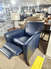 The Superstyle L74 Push-Back Reclining Chair graces the furniture store display room, offering unparalleled comfort. This luxurious leather recliner is surrounded by other couches and lamps, inviting you to experience the perfect blend of style and relaxation.