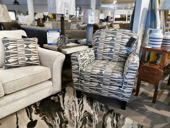 A Trendline 356 Chair next to a beige sofa in a store, accompanied by a side table and decorative items.