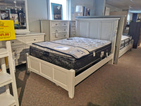 BB29552 Bonanza Bed, featuring a white bed frame with mattress, is displayed in a furniture store to highlight its transitional style. A dresser and mirror crafted from hardwood solids by Vaughan Bassett can be seen in the background, with a sale sign on the left enhancing its appeal.