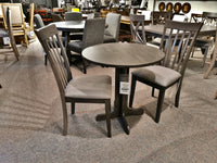 The DF30RD Delfini Dining Table Package by Winners Only features a small round table crafted from solid hardwood, paired with two wooden chairs upholstered in gray fabric, and is showcased in a furniture store to highlight its contemporary styling.