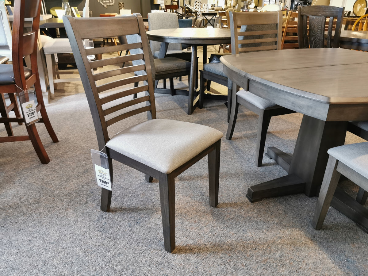 An Annapolis Side Chair from Winners Only, featuring a slatted back and cushioned seat with a dark chocolate finish, is showcased next to a matching table made of solid hardwood in a furniture store.