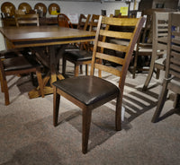 The Newport Dining Set by Winners Only includes a dining chair featuring transitional styling, with a solid hardwood frame and a dark cushioned seat. It sits gracefully on a carpeted showroom floor among other furniture, hinting at durability and timeless elegance.