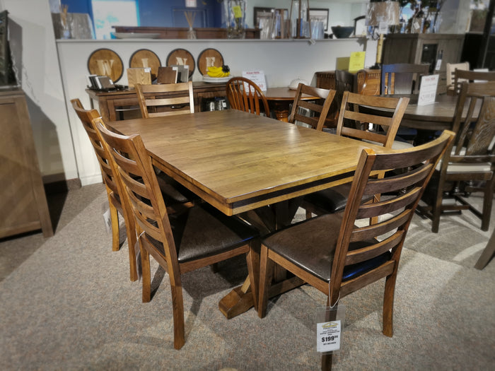 The Winners Only Newport Dining Set, featuring a solid hardwood dining table with a distressed finish and six chairs, is elegantly displayed in a furniture store. Price tags are attached to both the table and the chairs, highlighting its exquisite transitional styling.