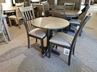 The DF30RD Delfini Dining Table Package by Winners Only, featuring a round wooden table with three chairs crafted from solid hardwood, is on display in a store. The set showcases contemporary styling and includes attached price tags.