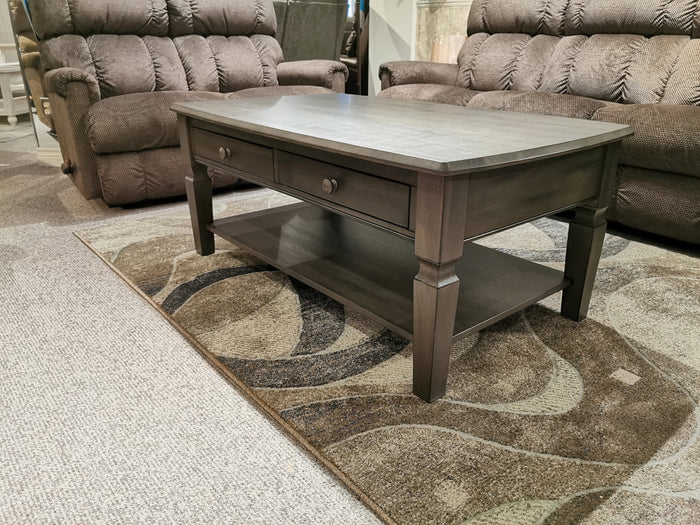 The Annapolis 48" Coffee Table by Winners Only, crafted from solid hardwood with a rich dark wood finish, features two drawers and a shelf. It complements the contemporary style beautifully as it rests on a patterned rug nestled between two brown recliners.