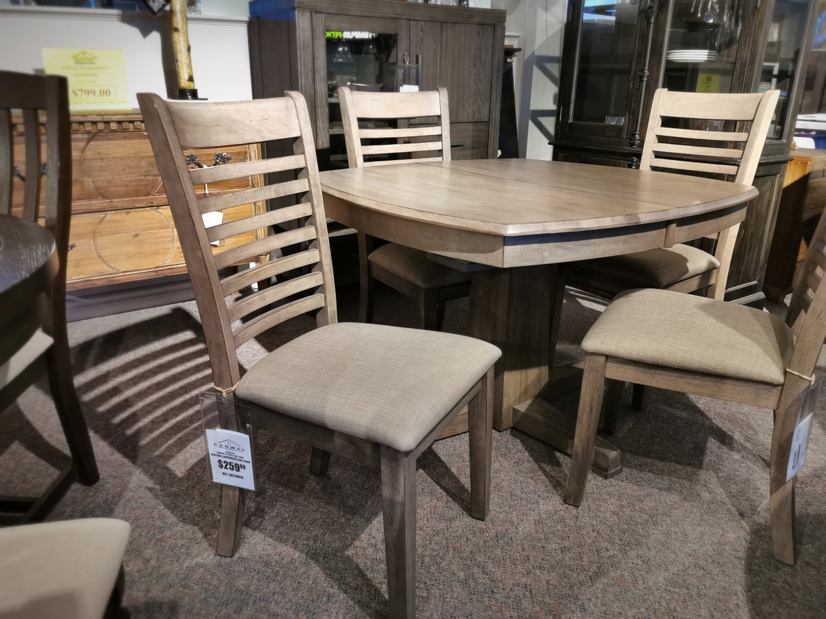 The Ventura Dining Package by Winners Only, a wooden dining table with four matching chairs featuring cushioned seats and a stylish grey washed finish, is displayed in a furniture store.