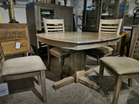 The Ventura Dining Package by Winners Only features a wooden round dining table crafted from solid hardwood and includes four matching chairs. Displayed on a carpeted floor in a furniture showroom, this elegant piece exudes natural charm and timeless appeal as part of the Santa Fe collection.