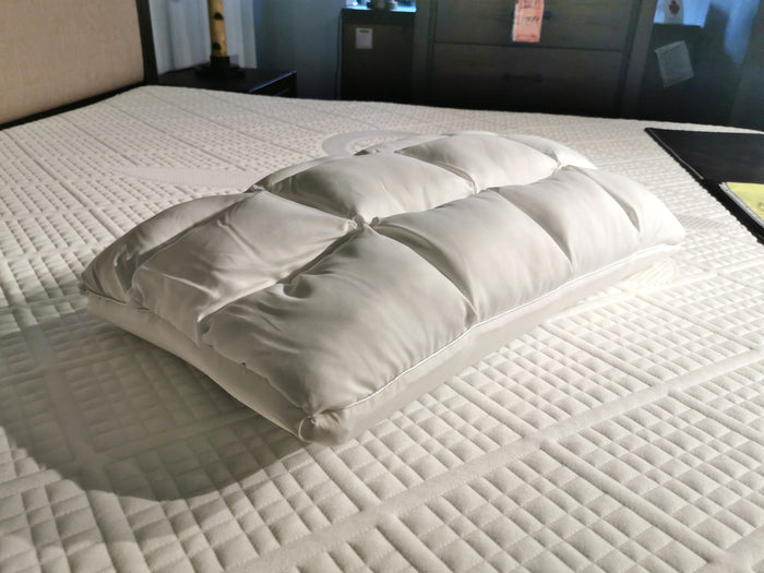 A SUB-0 Hybrid Pillow by Zucora Home, featuring a white quilted design with Cooling Gel, rests on a patterned mattress in a cozy bedroom setting.